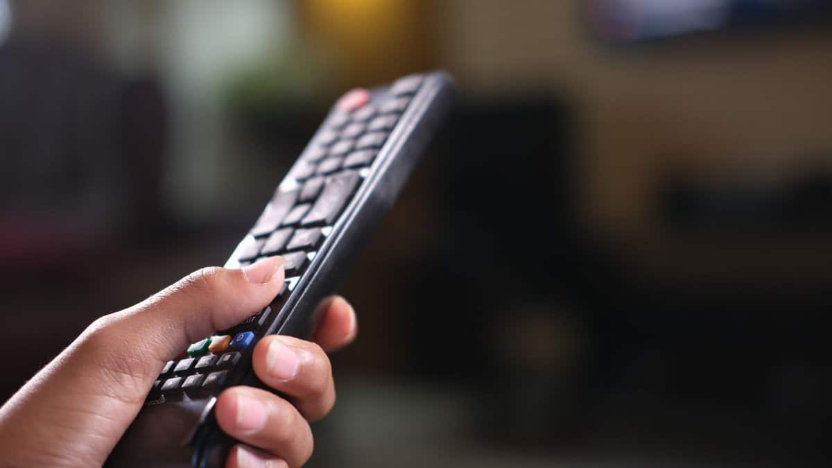 Hand holding a TV remote control, focusing on buttons and grip indoors.