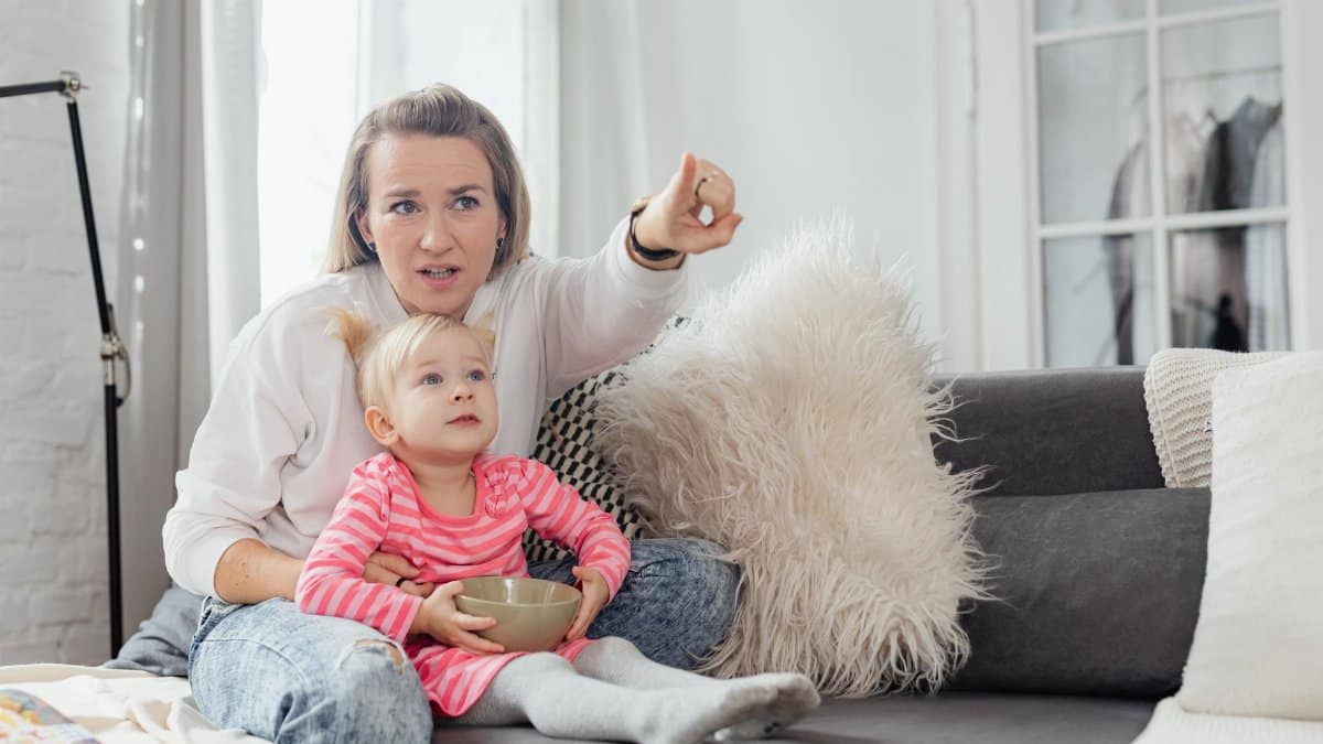 A mother and daughter enjoying quality time on the couch, pointing and watching TV together.