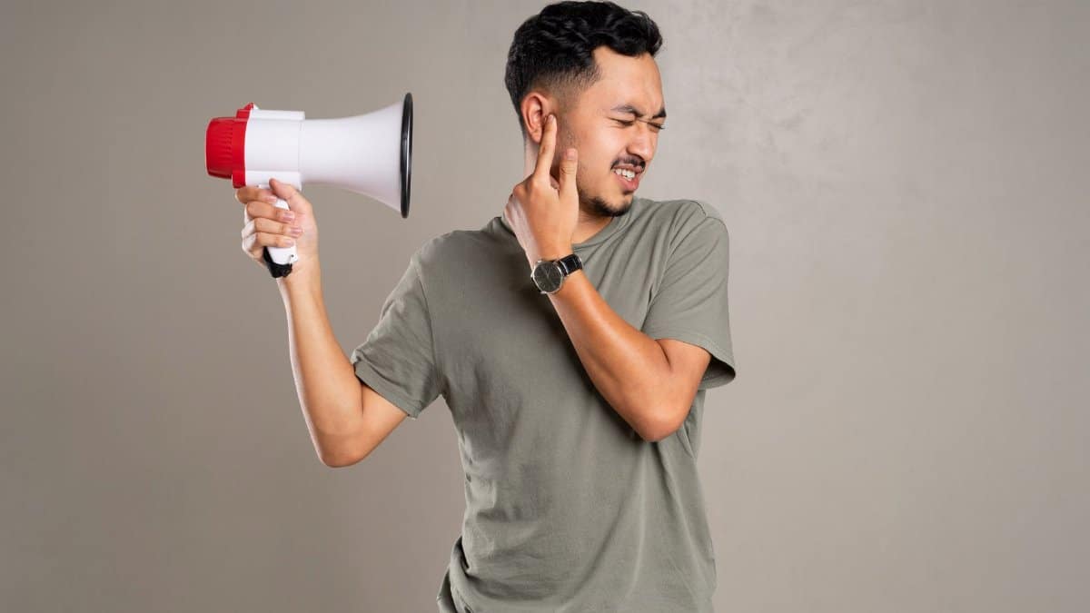 A man with a megaphone holding ear in discomfort, representing noise pollution or loud sounds.