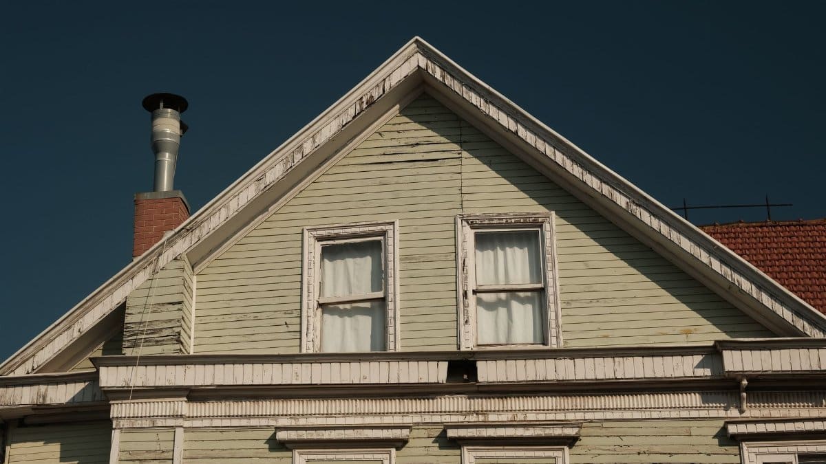 A close-up of an old wooden house facade with a chimney under a clear sky.