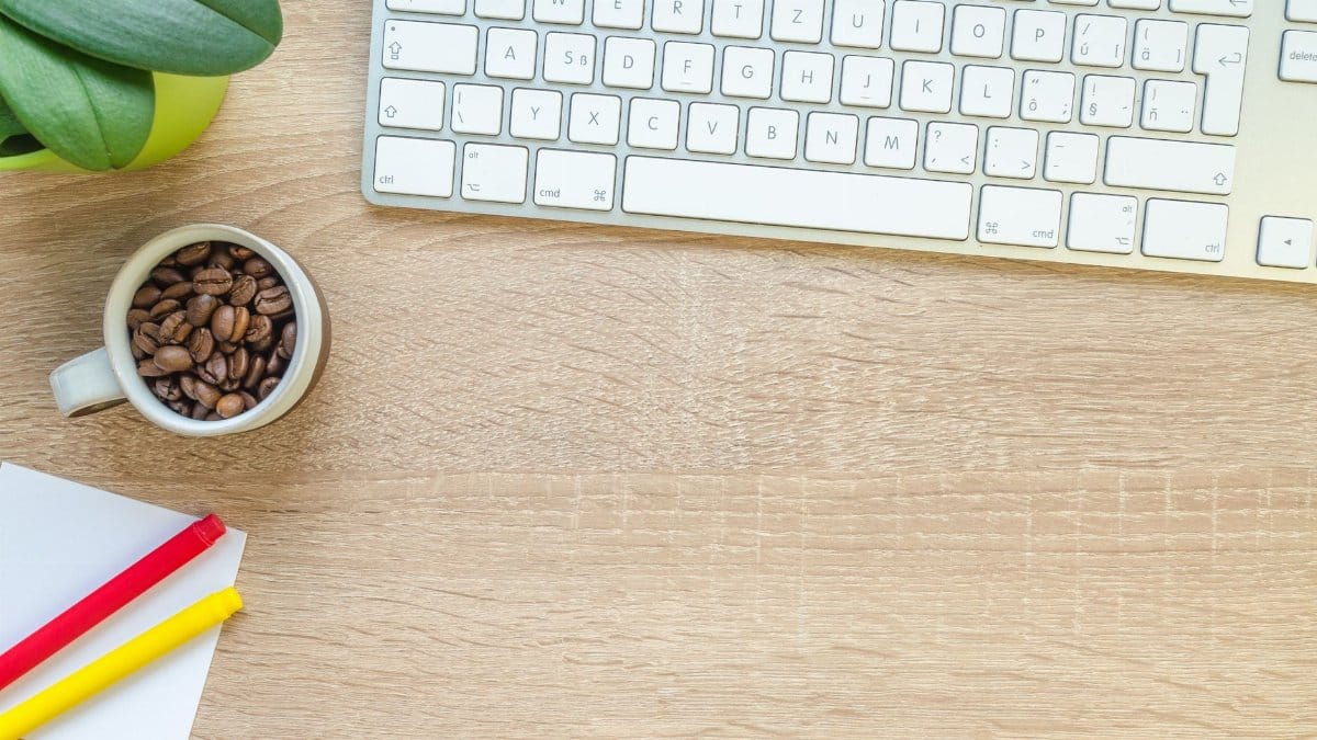 Overhead view of keyboard, coffee beans, and stationery on a wooden desk.