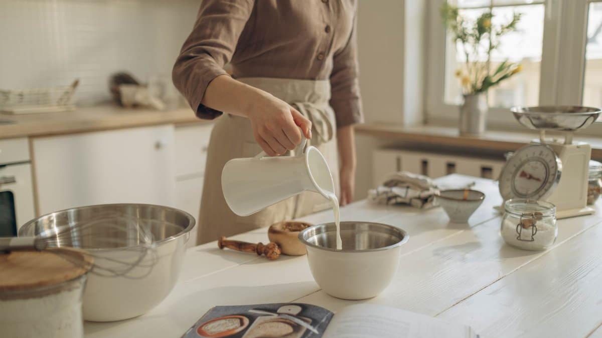 A person pours milk into a bowl, preparing ingredients on a kitchen island for baking.