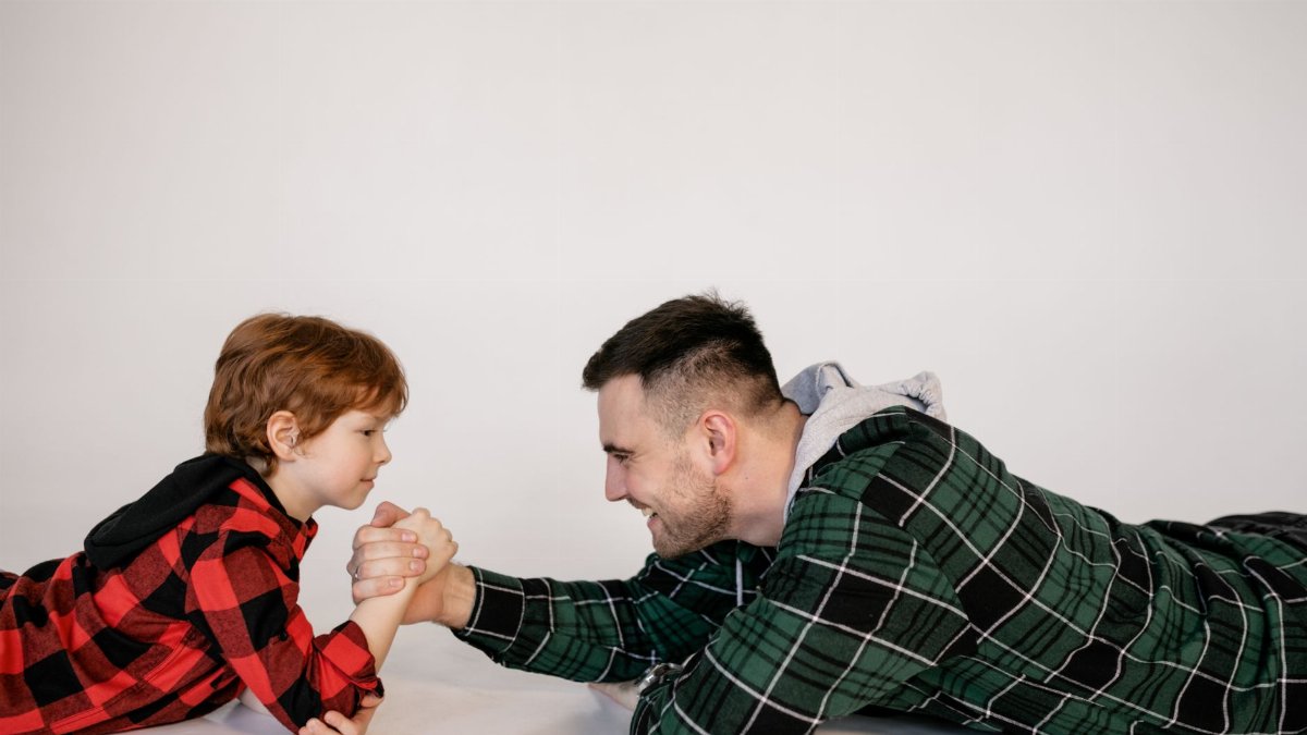 A warm moment of father and son arm wrestling in plaid shirts, smiling and bonding indoors.
