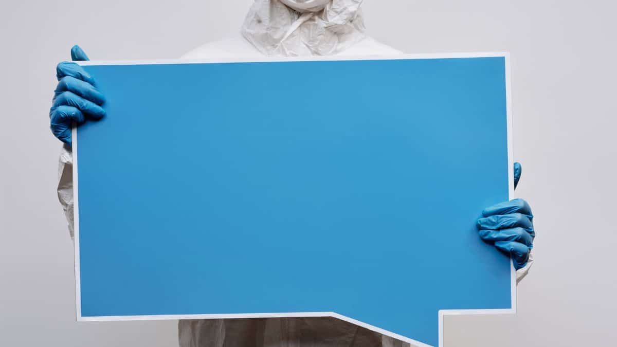 A person wearing protective gear holding a large blue speech bubble placard with copy space.