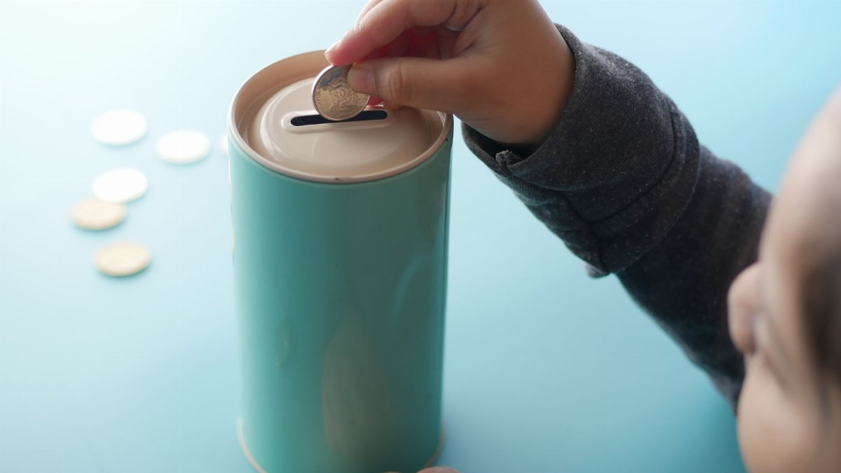 A child placing a coin into a teal piggy bank, representing saving money and financial education.