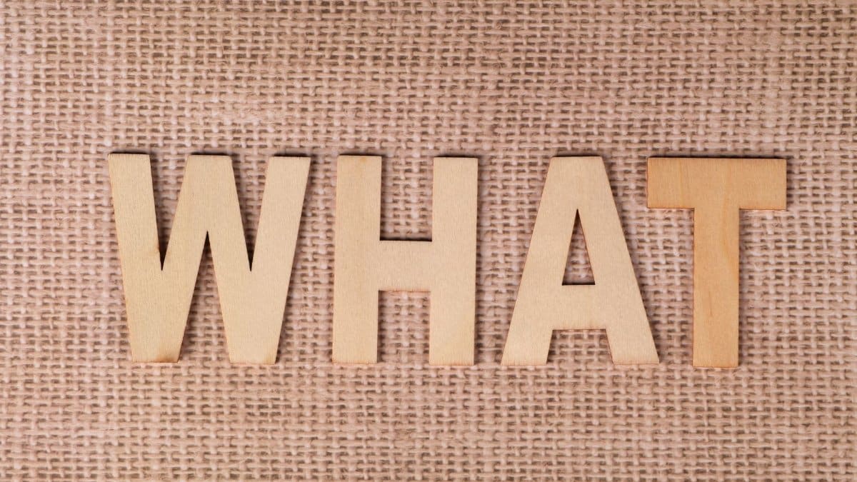 Wooden letters forming the word WHAT set on a textured burlap surface.