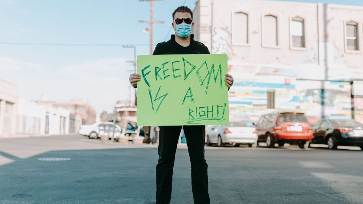Man wearing face mask holding a sign reading 'Freedom is a Right!' during a street protest.