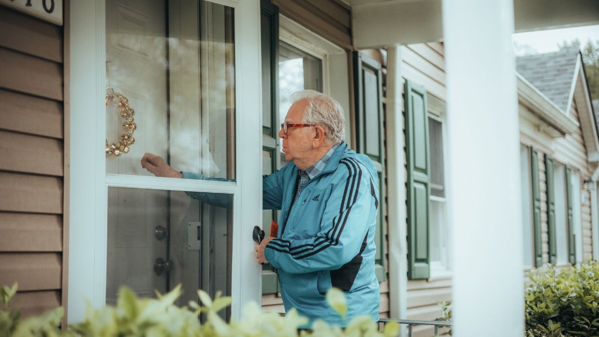 Elderly man in a blue jacket knocking on a suburban house door, showcasing community life.