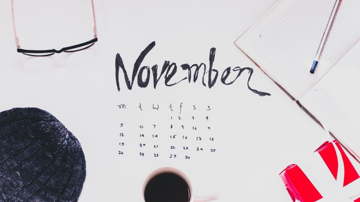 Flat lay of a November calendar with cozy autumn accessories, warm sweater, and hot coffee.