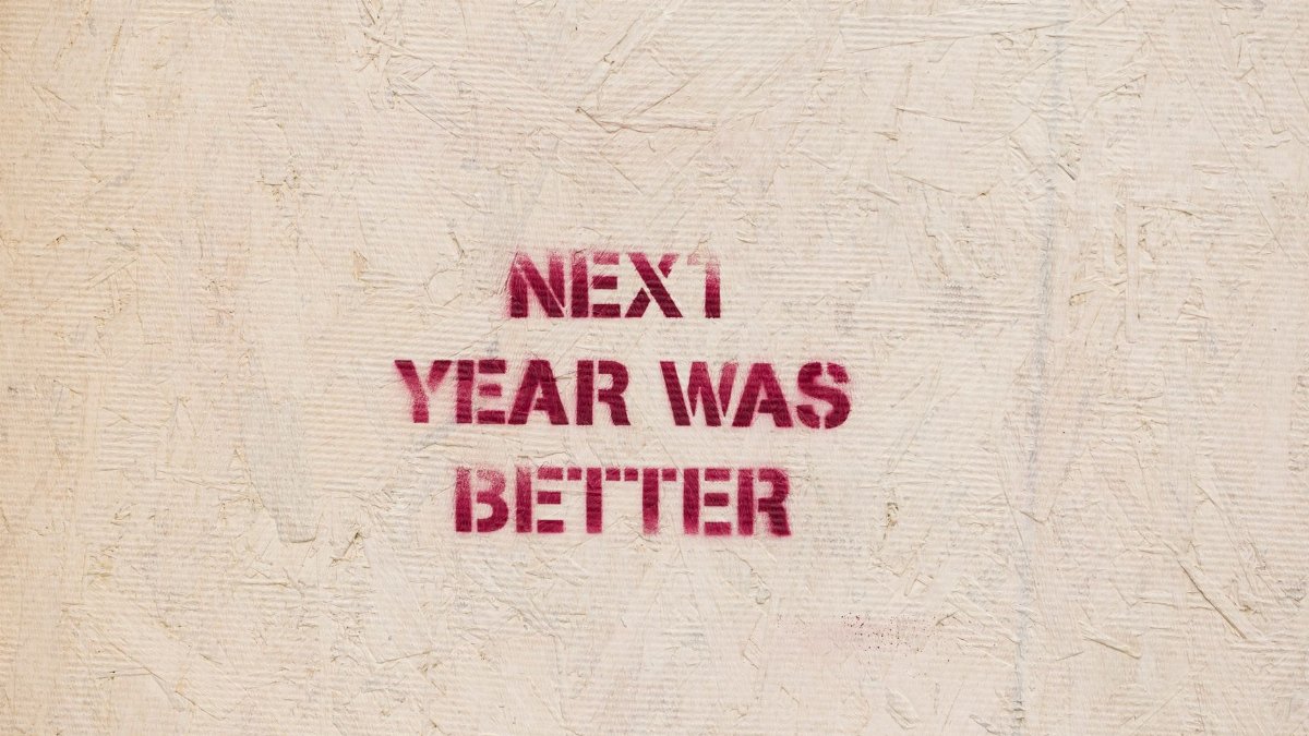 Rustic wall art with an inspirational message 'NEXT YEAR WAS BETTER' stenciled on a textured surface.