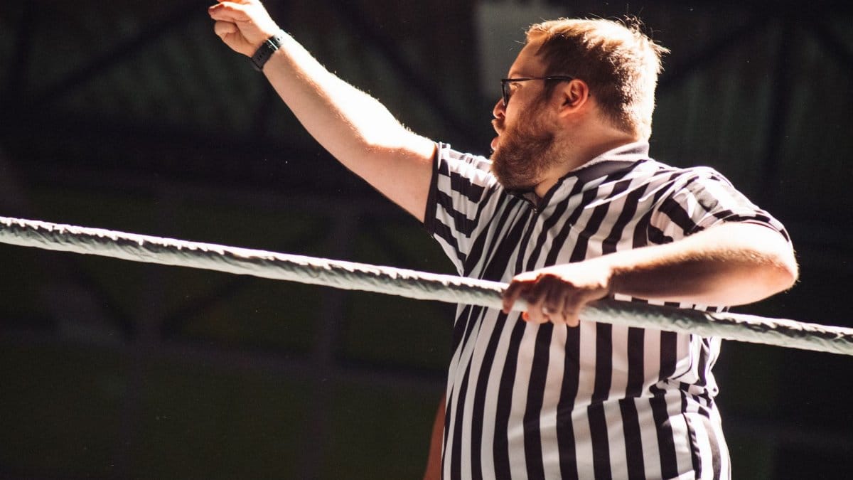 Referee signaling during an intense wrestling match, indoors.