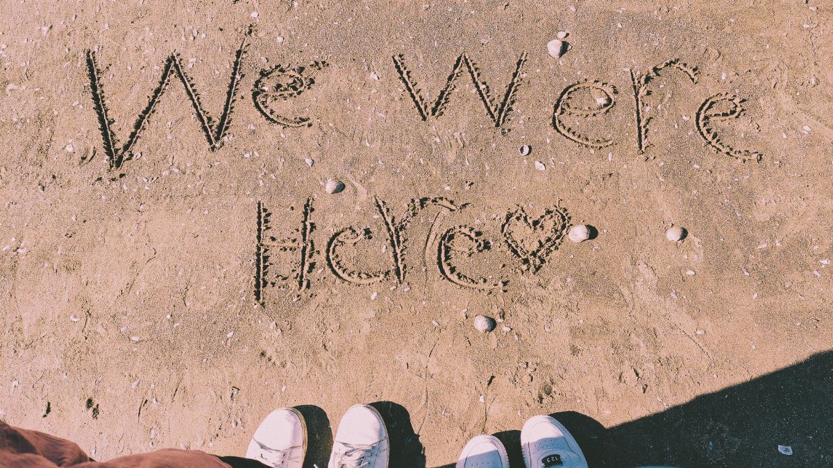 Beach sand with 'We Were Here' text and people's shoes in Port Said, Egypt.