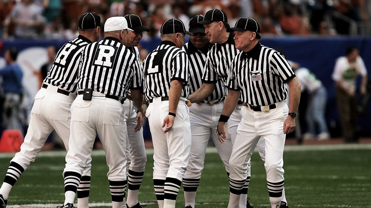 Team of referees discussing a play during a football game in a vibrant stadium.