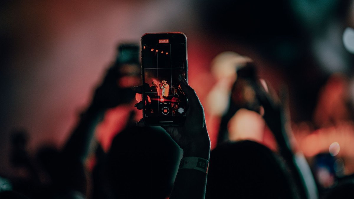 A close-up of a smartphone recording a lively concert scene with colorful stage lights.