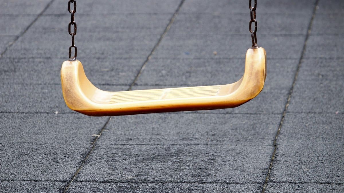 Close-up of a yellow swing on a playground with rubber mat flooring.