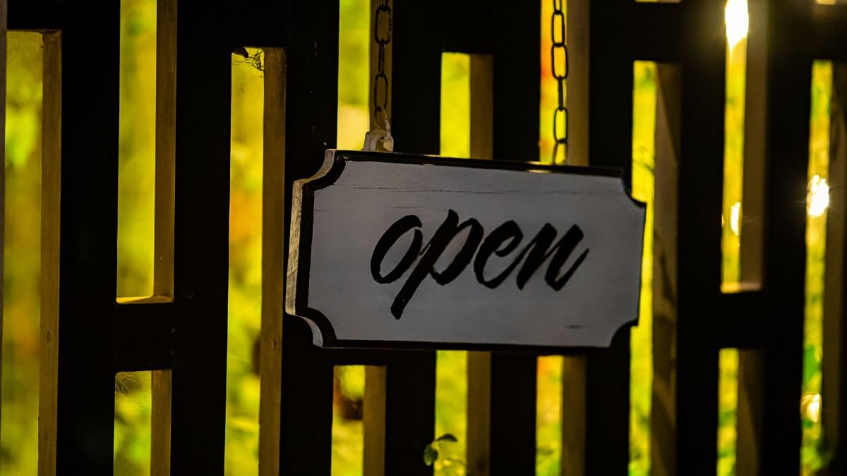A warmly lit 'open' sign hanging on a wooden fence at night creates a welcoming atmosphere.