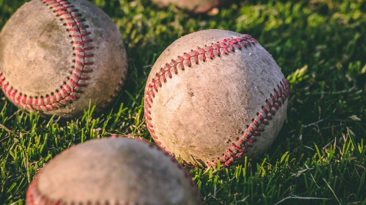 Close-up of multiple baseballs lying on a grassy field in bright sunlight.