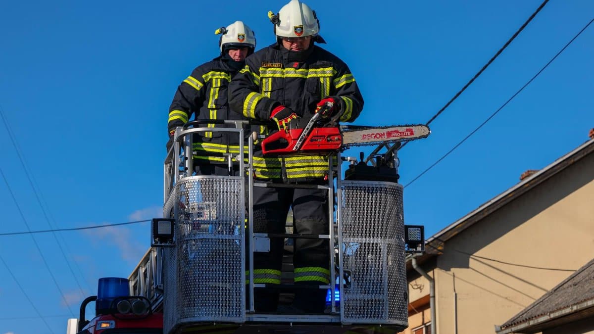 Firefighters in action on a ladder truck, using a chainsaw for rescue operations under a clear blue sky.