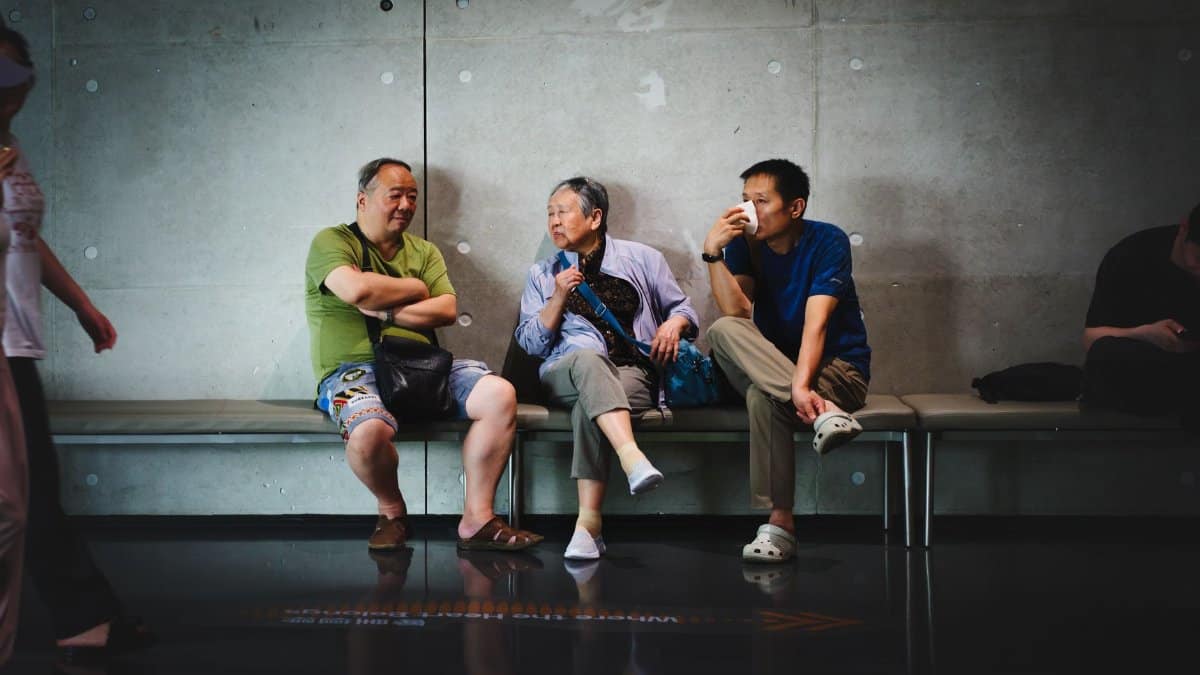Three adults engage in casual conversation while sitting on an indoor bench.