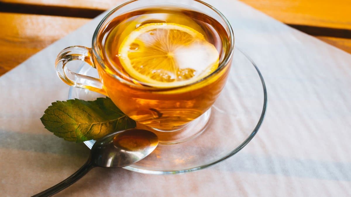 Close-up of lemon tea in a glass teacup with mint leaves and a spoon on a wooden table.