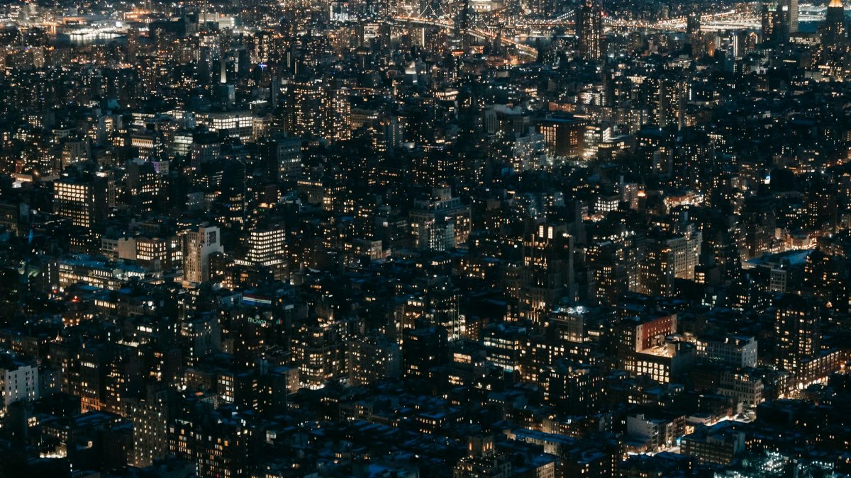 Drone view of modern multistory buildings with glowing lights located on dark streets of contemporary city at dark night time