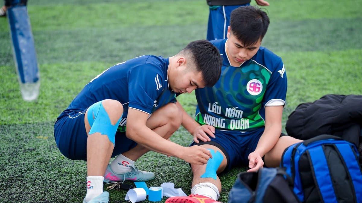 Football players applying kinesiology tape on the field in Hà Nội, Vietnam.