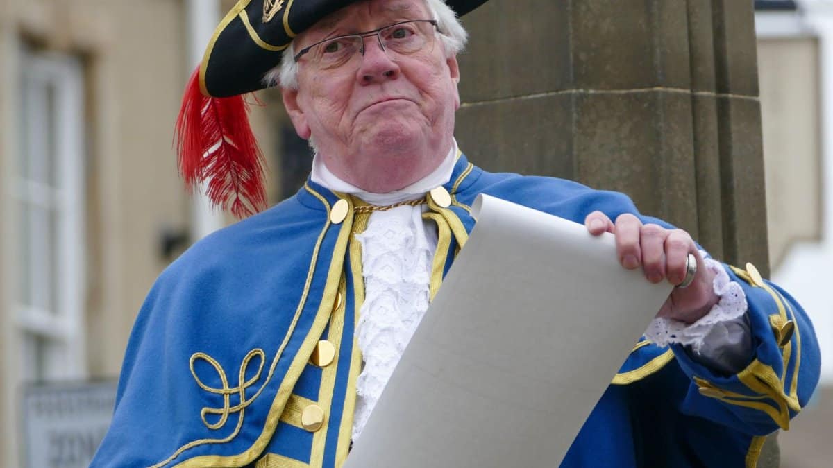 A town crier in traditional costume and tricorne hat holding a scroll in Knaresborough, England.