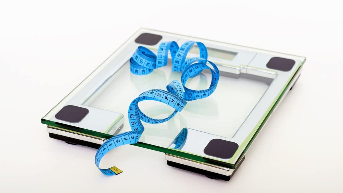 A digital glass weighing scale with a blue measuring tape, symbolizing weight management.