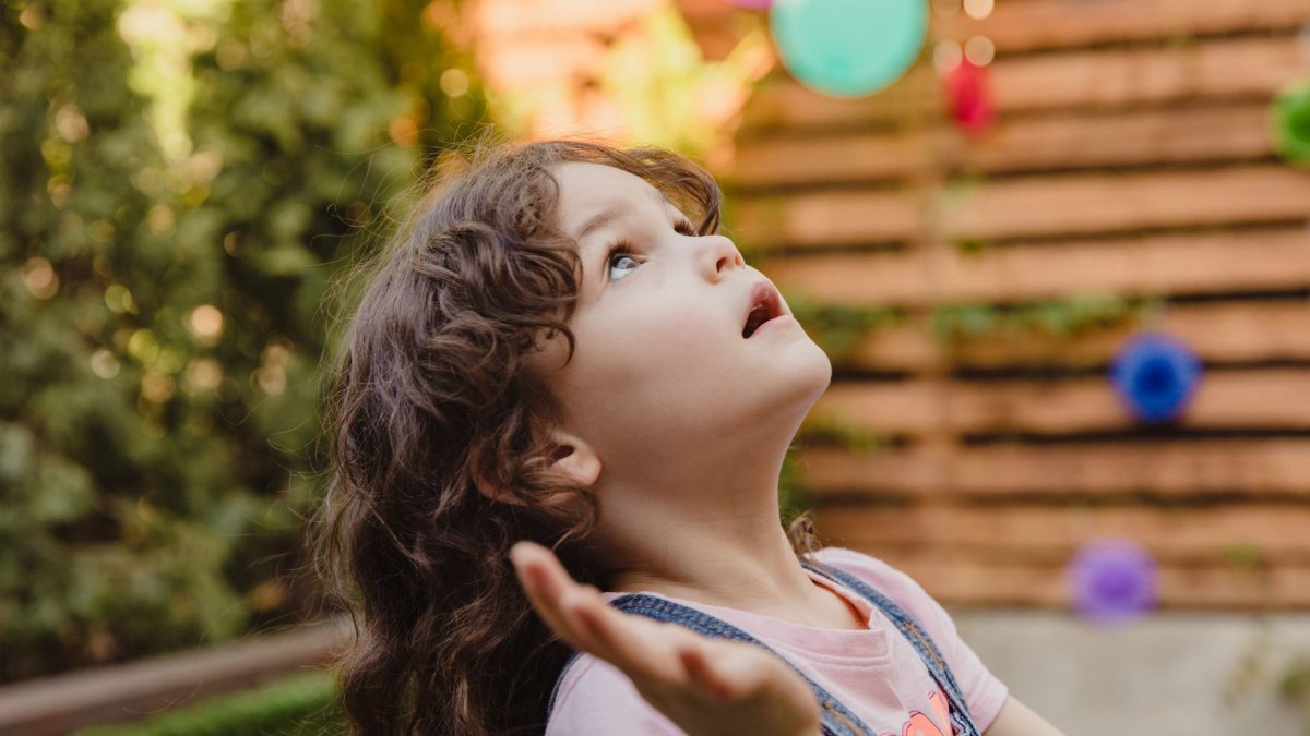 A child gazes up at colorful balloons in an outdoor setting, evoking wonder and innocence.