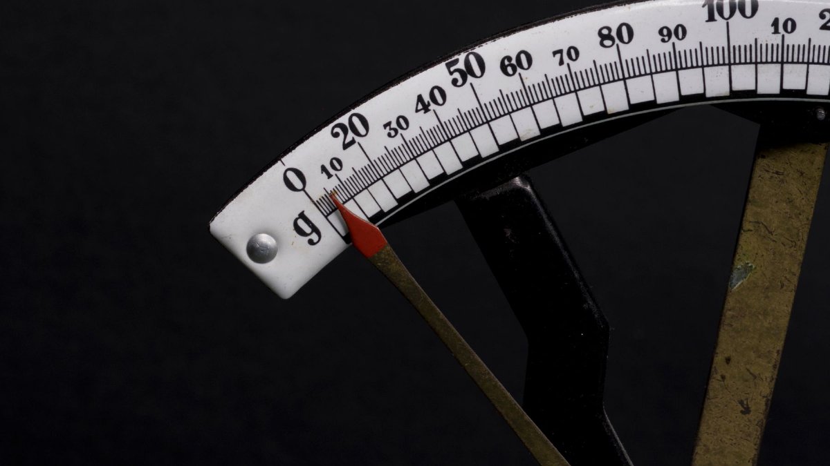 Detailed close-up image of a vintage analog weighing scale with a pointer against a black background.