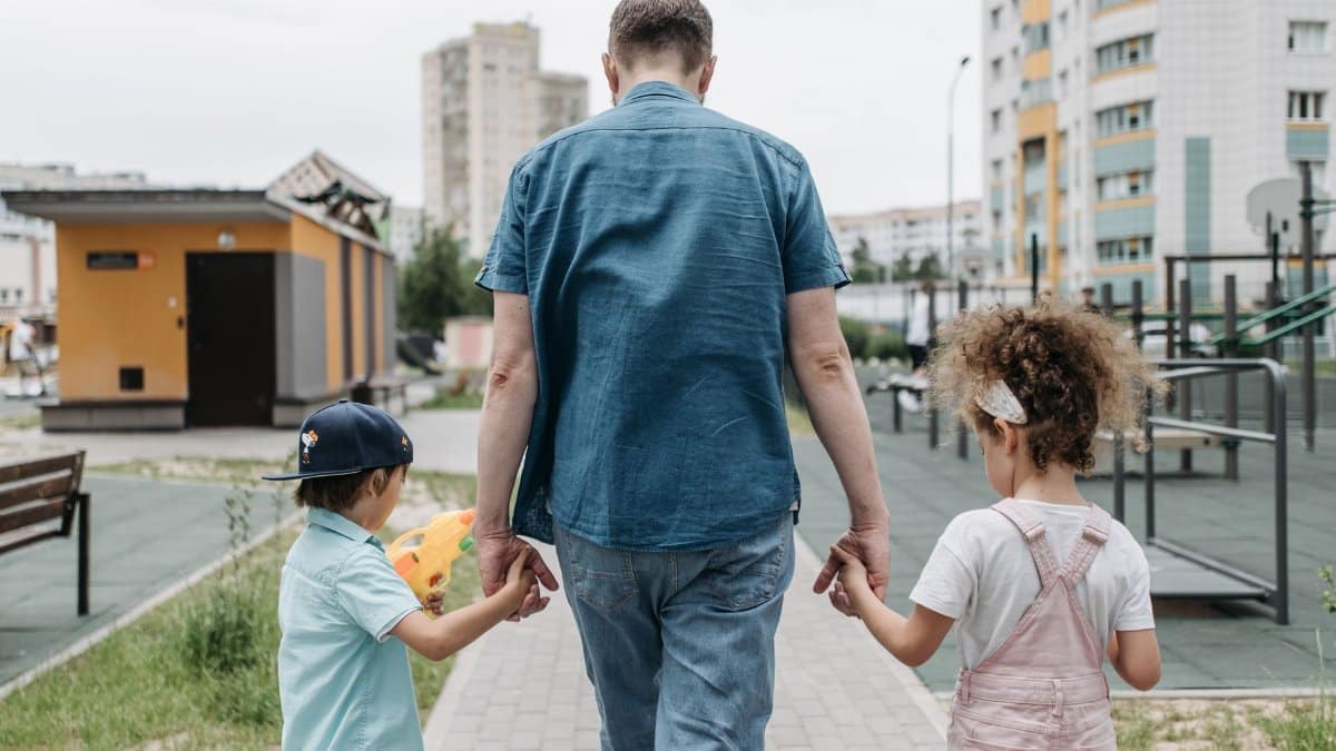 Father and children holding hands, enjoying a walk in a city park.