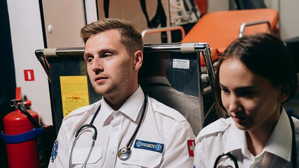 Two paramedics sitting in an ambulance, equipped with stethoscopes and emergency tools.