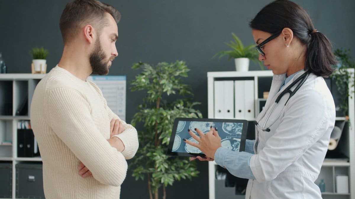 A doctor shows MRI scan to a worried patient using a tablet in a modern clinic.