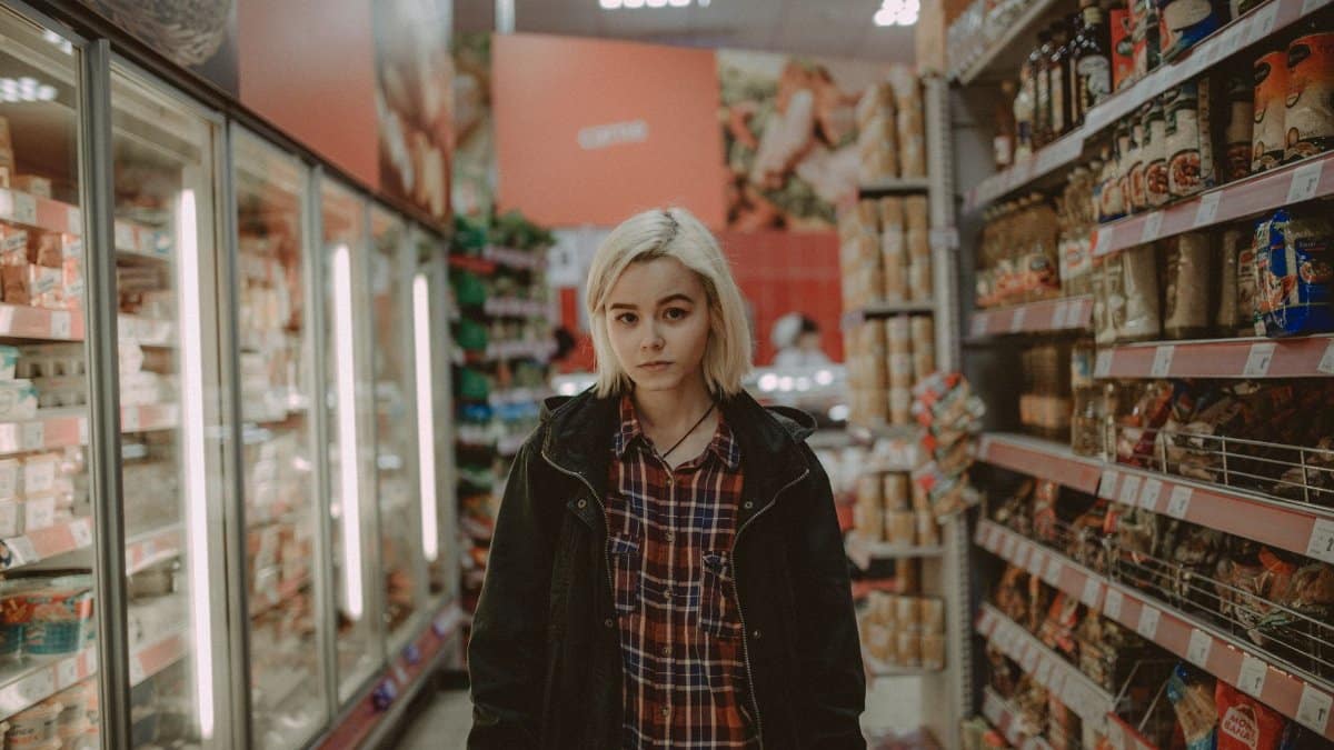 A woman with white hair stands between shelves in a supermarket aisle, showcasing a variety of products.