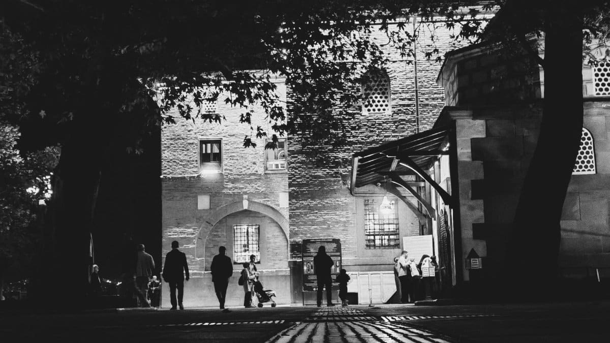 Black and white photo capturing people walking near a historic building at night.