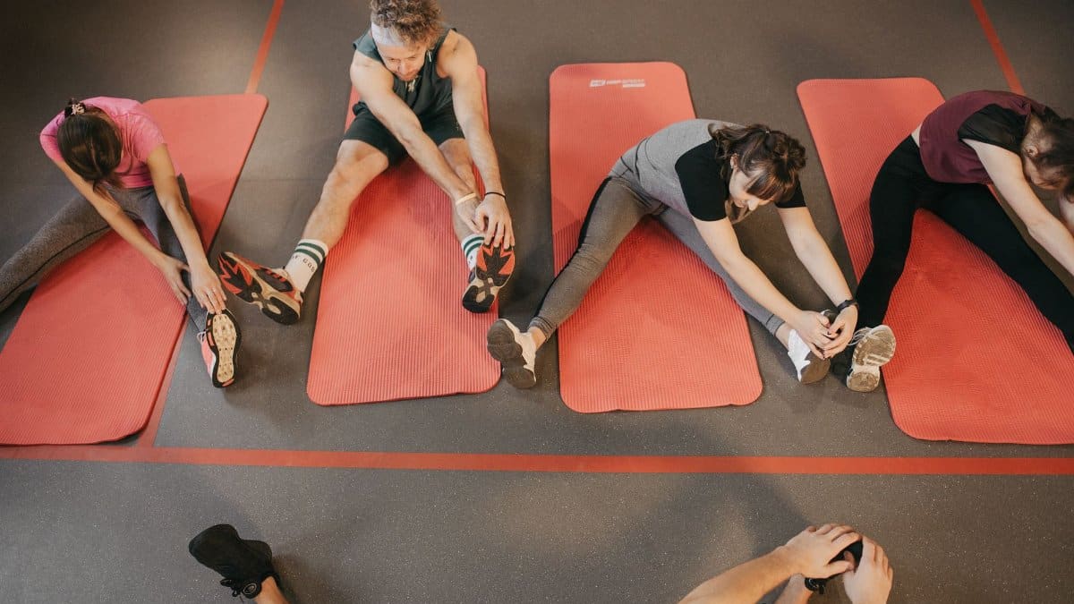 Four people stretching on red mats during a group exercise session indoors.
