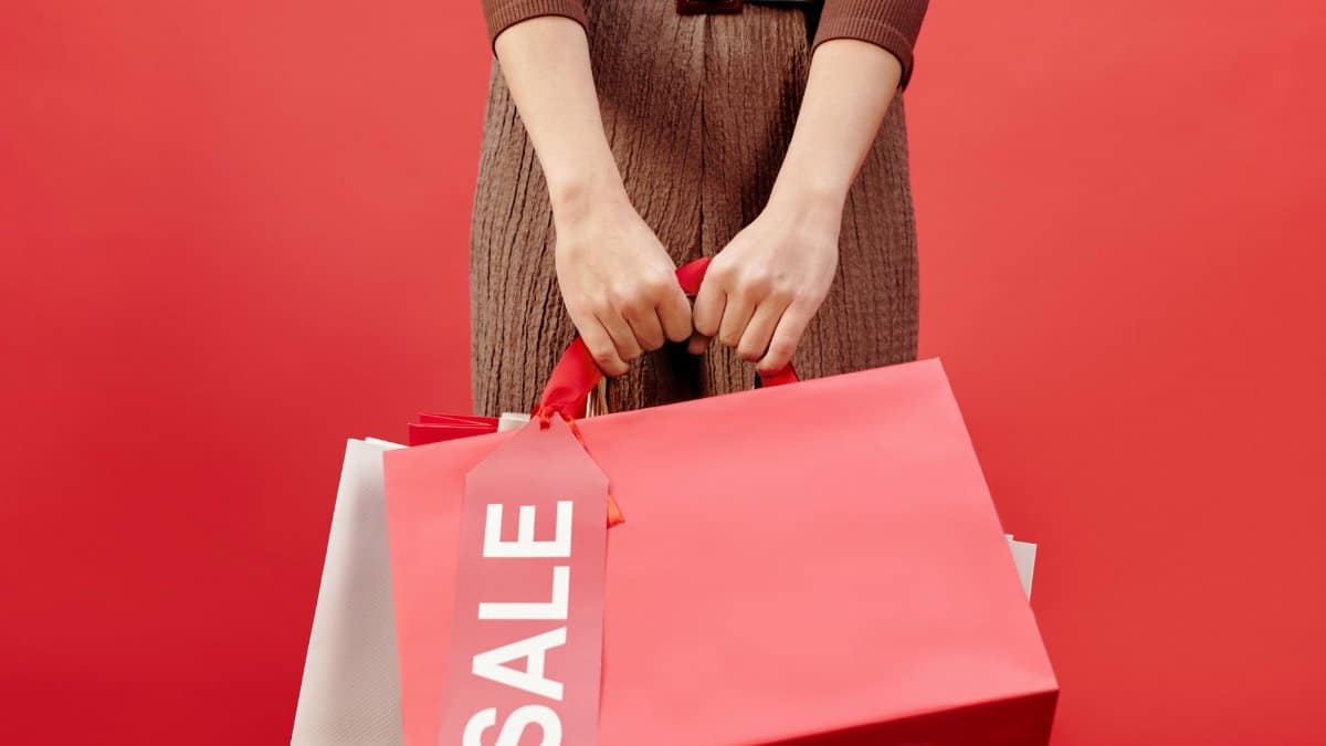 Close-up of a person holding shopping bags with a sale tag on a red background.