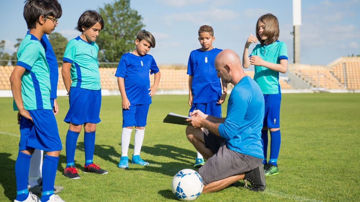 Coach guiding young soccer players on a lush green field under a clear sky.