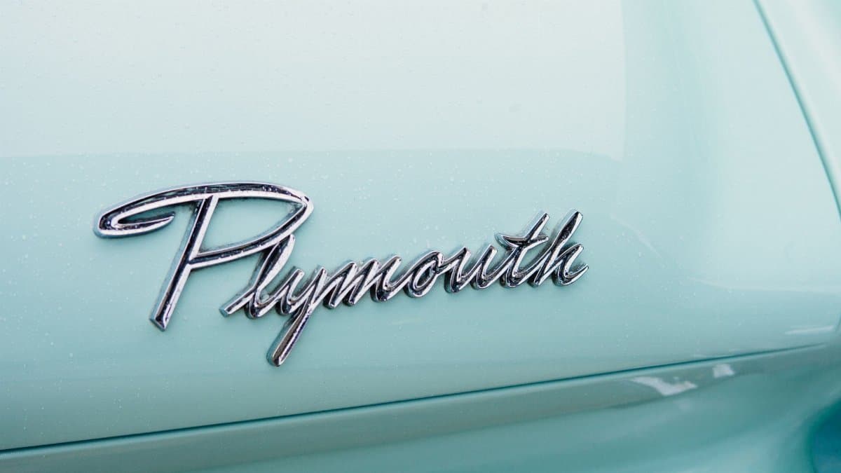 Chrome Plymouth emblem on vintage car with light blue paint and sleek design.