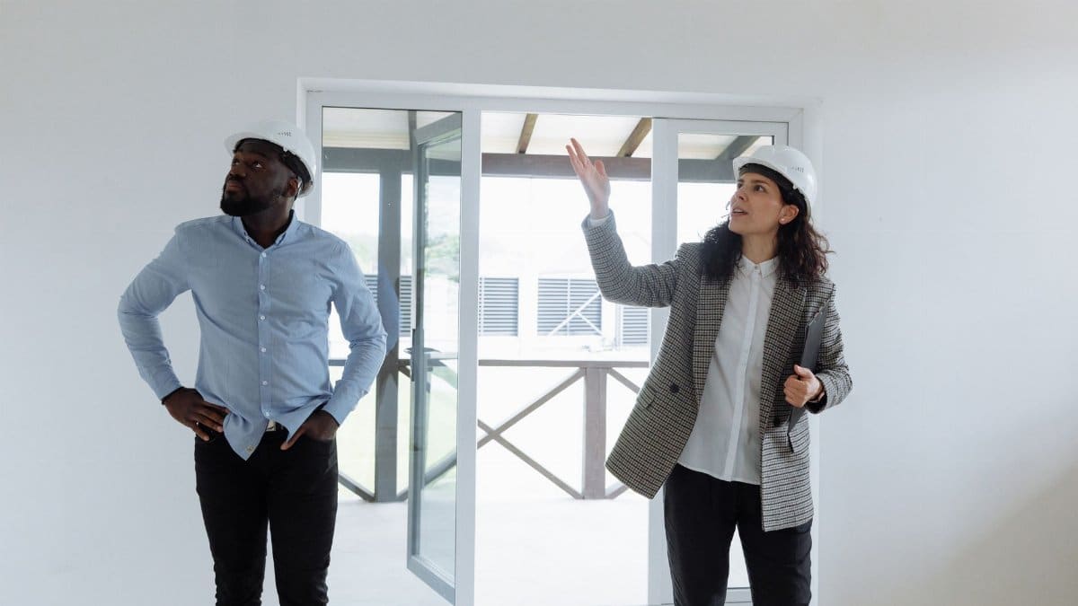 Two contractors inspecting a modern house interior wearing hard hats.