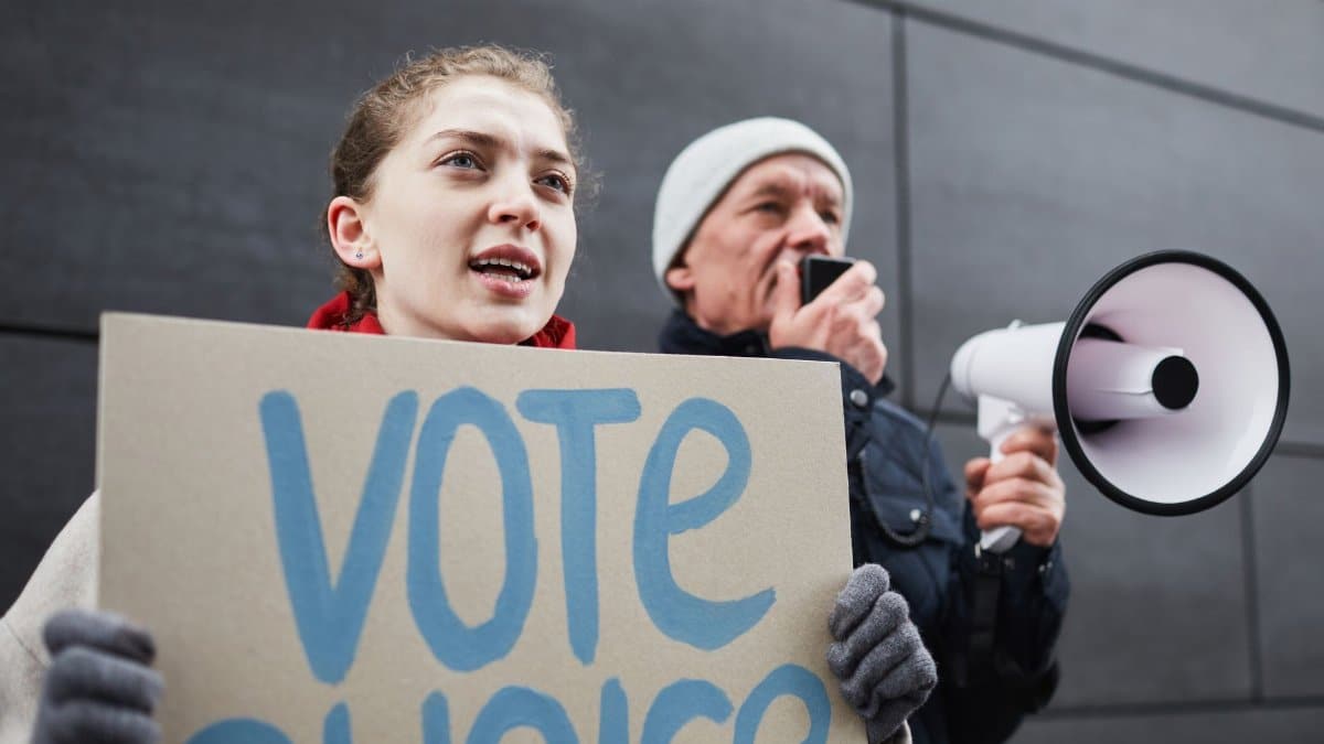 Two adults protesting with a 'Vote Choice' placard and megaphone in an urban setting.