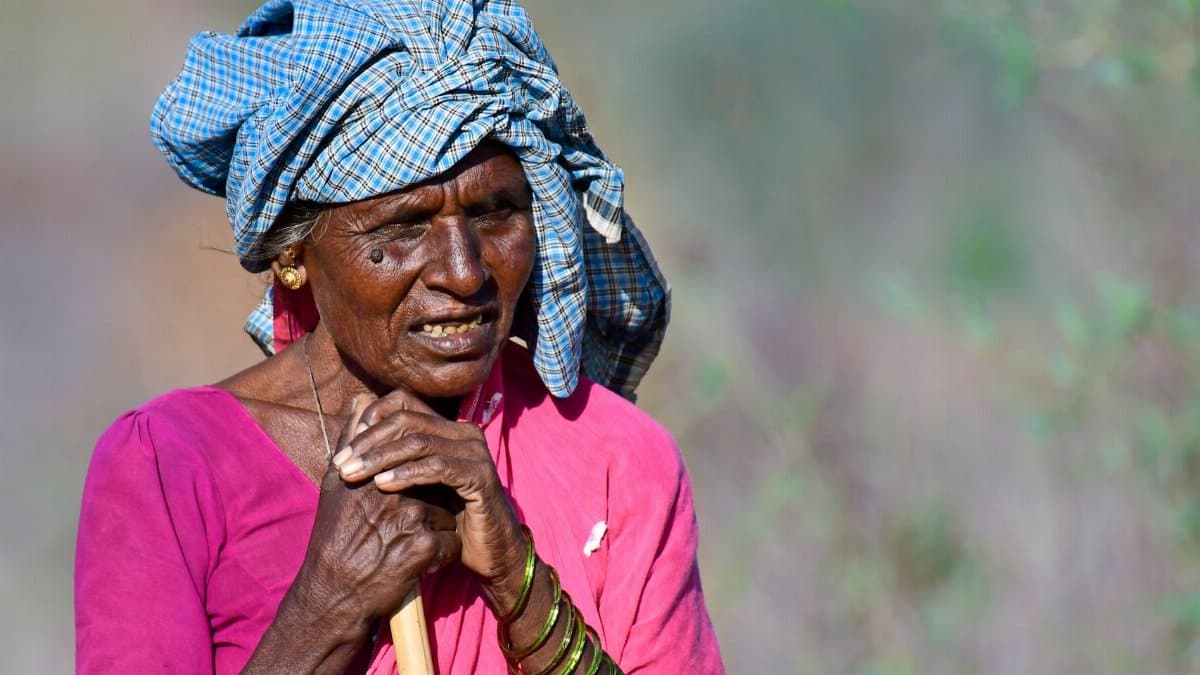 Portrait of an elderly woman wearing a traditional headscarf and colorful dress standing outdoors.