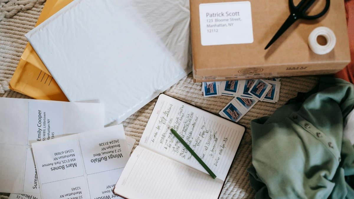 Top view arrangement of opened notebook placed near carton parcel near postage stamps envelops and address labels