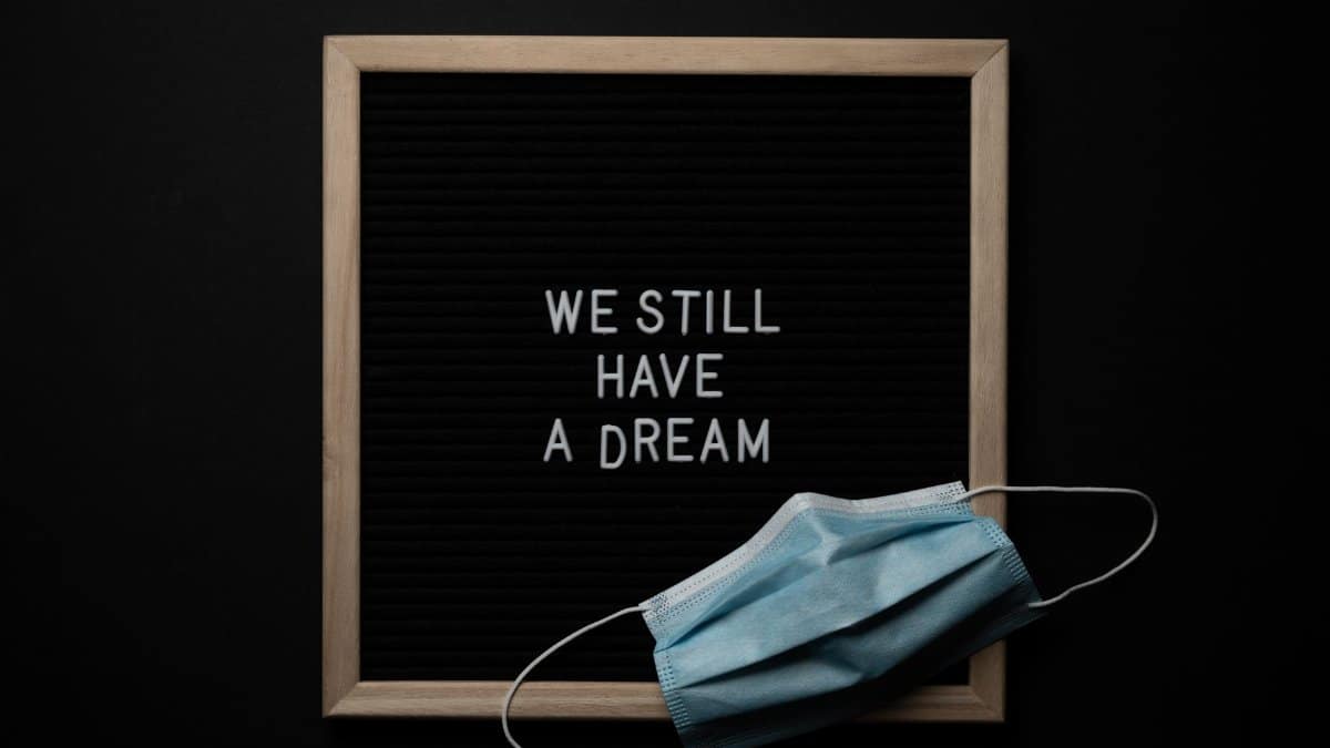 Blackboard with wooden frame with white We Still Have a Dream inscription and medical mask placed on black background