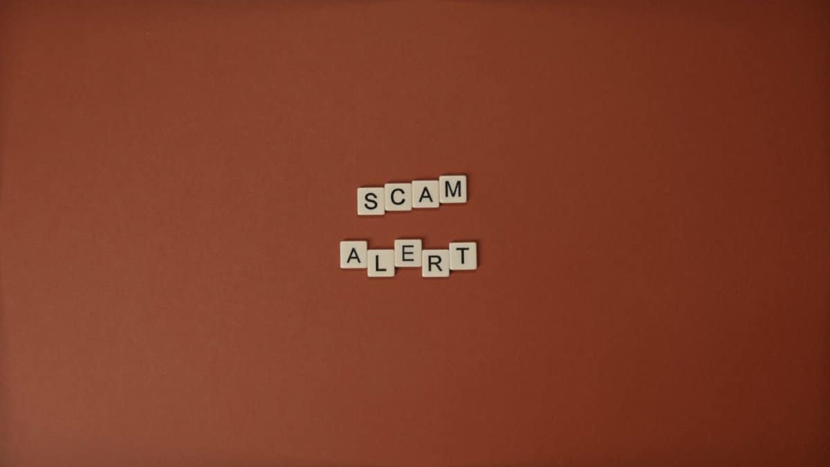 Scrabble tiles spelling Scam Alert on a brown surface indicating caution.