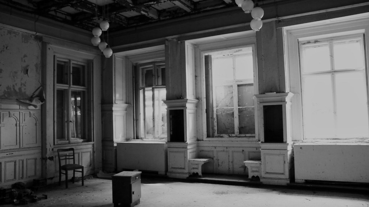 Eerie abandoned room with hanging lights, showcasing decaying architecture in grayscale.