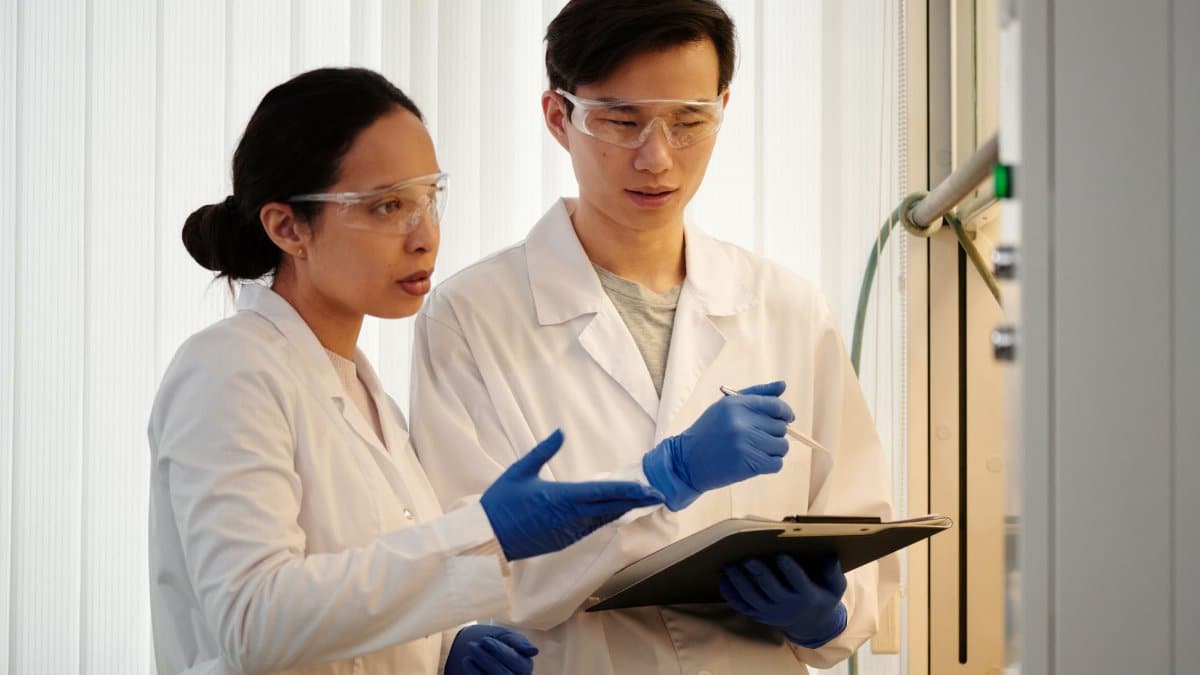 Researchers discussing data in a laboratory setting, wearing safety gear and blue gloves.