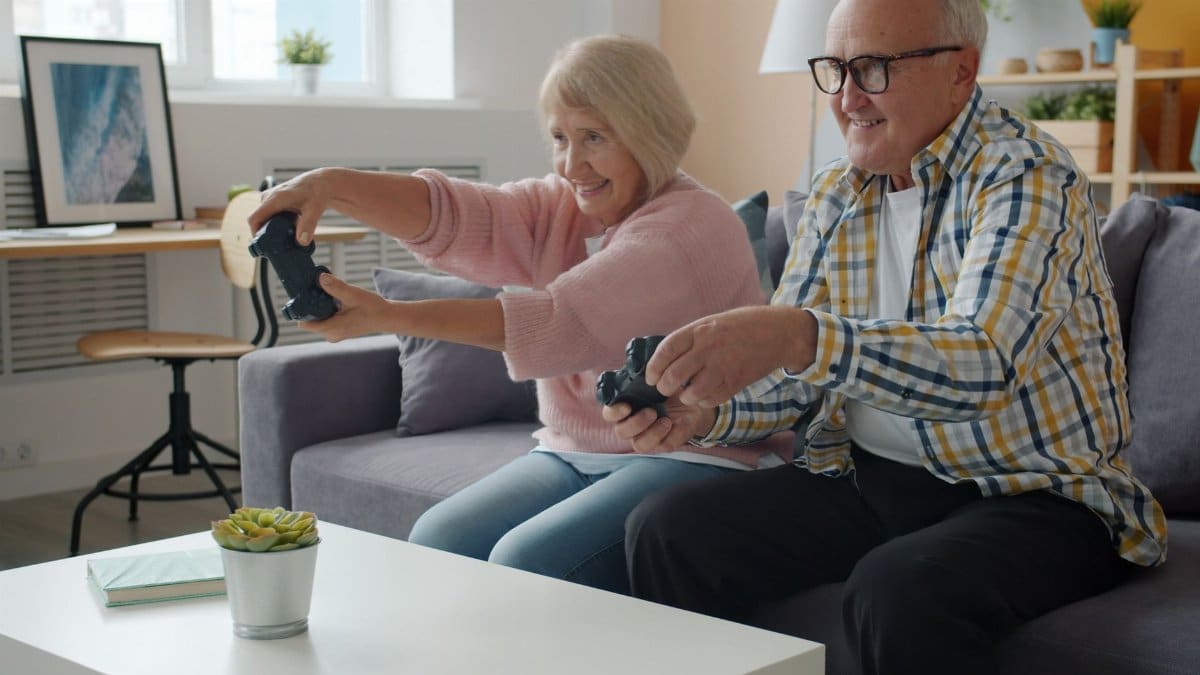 Happy senior couple playing video games on a couch, having fun indoors.