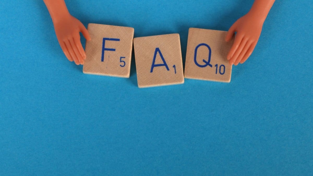 Flat lay of scrabble tiles spelling 'FAQ' with toy hands on a blue background, creating a conceptual image.