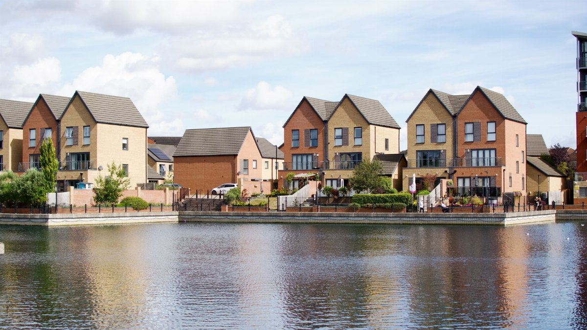 Row of modern houses by a lake with clear reflections and blue sky.